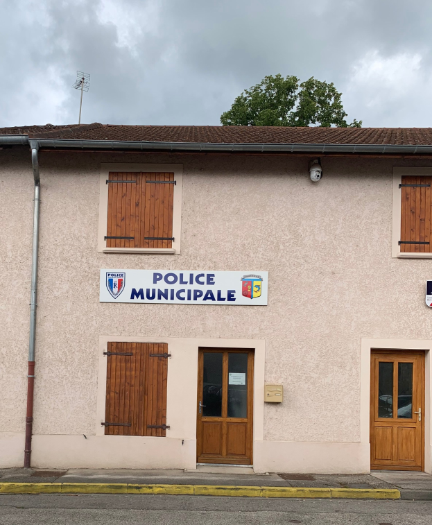 Polizeigebäude mit einem Schild, Fenstern, Türen, einer Namensschilder, einem Rohr, einem Baum und einem bewölkten Himmel im Hintergrund.