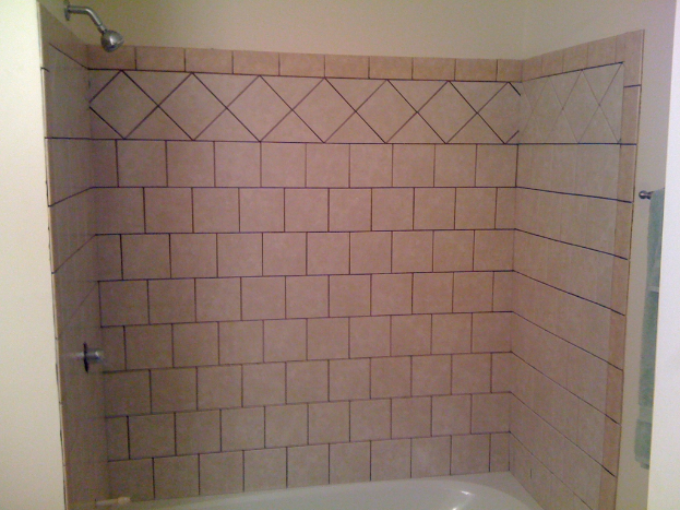Eine Ziegelwand mit einer Dusche, einem Wasserhahn und einer Badewanne; ein Handtuch hängt an einem Haken an der linken Seite.