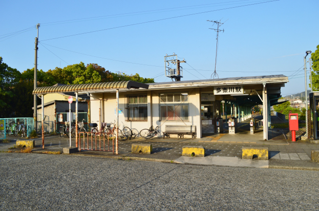 Ein Bahnhof mit Fahrrädern davor, eine Straße unten und Häusern, Bäumen, Polen, Drähten und einem klaren blauen Himmel im Hintergrund.