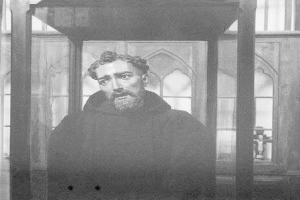 Ein Schwarz-Weiß-Foto eines bärtigen Mannes in einem langen Gewand, der vor einem offenen Fenster steht, sein Gesicht von natürlichem Licht erhellt.