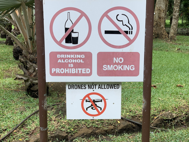 Schilder am Straßenrand mit der Aufschrift "Alkoholgenuss ist untersagt" und "Rauchen verboten", mit Bäumen und Gras im Hintergrund.