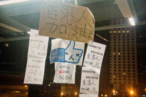 Menschen vor einem beleuchteten Gebäude bei Nacht mit Schildern an der Decke, wahrscheinlich protestierend gegen ein Social-Media-Verbot.