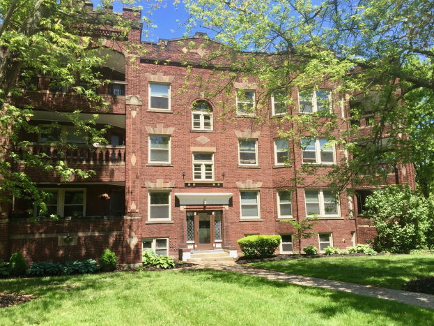 Großes Ziegelsteinhaus mit einem grünen Rasen, Bäumen und Pflanzen davor, unter einem klaren blauen Himmel, gelegen in Chicago, Illinois.