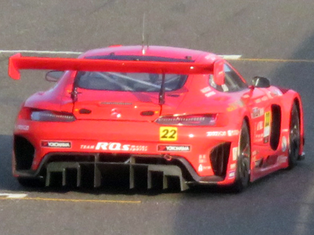 Roter Porsche 911 GTS Rennwagen auf einer Rennstrecke mit großem Heckspoiler und Flügel, schwarzen Rädern und aerodynamischem Design.