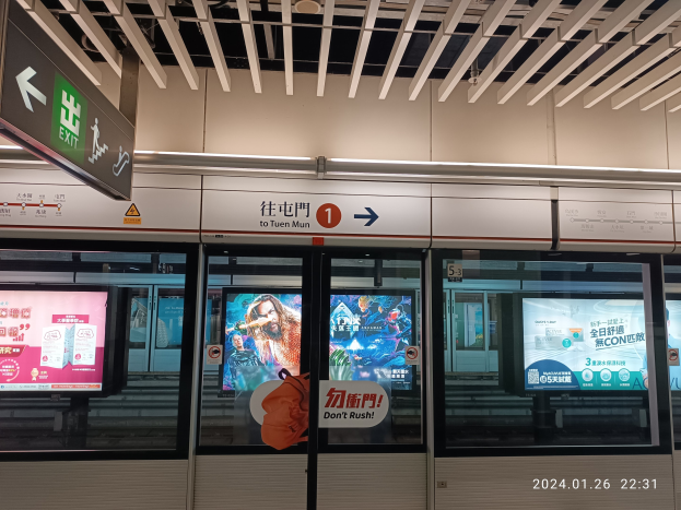 U-Bahn-Zug an einer Station mit Glastüren, Bildschirmen und digitaler Anzeige neben Tafeln mit Text und Zahlen an der Wand unter Deckenbeleuchtung.