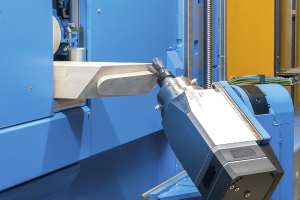 CNC-Fräsmaschine schneidet ein Holzstück in einer Fabrikumgebung, umgeben von Kabeln und anderen Gegenständen mit einer Wand im Hintergrund.