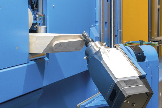 CNC-Fräsmaschine schneidet ein Holzstück in einer Fabrikumgebung, umgeben von Kabeln und anderen Gegenständen mit einer Wand im Hintergrund.