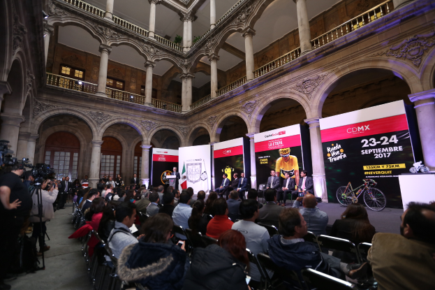 Eine Gruppe von Menschen an einem Tisch mit einem Podium und einem Mikrofon vor einer Menge, Kameras und Bannern während einer Pressekonferenz für das CDMX 2017-Event.