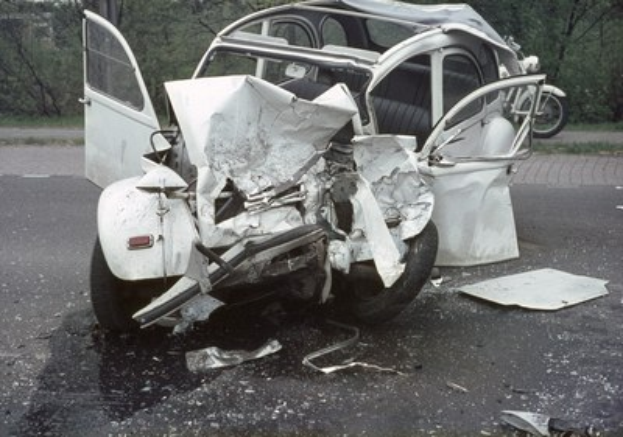 Schwer beschädigt: Front eines Wagens nach Crash am Straßenrand, Bäume und Gebäude im Hintergrund sowie ein weiteres Fahrzeug in der Ferne.