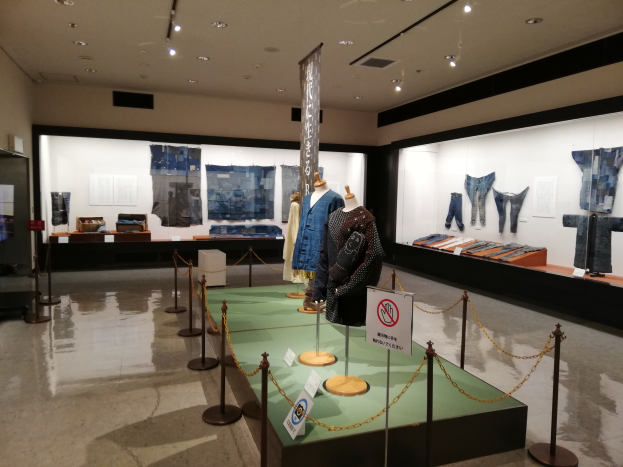 Eine Museumsausstellung mit Puppen in traditioneller japanischer Kleidung, Vitrinen voller verschiedener Kleidungsst├╝cke, Informationsschilder und Deckenlampen.