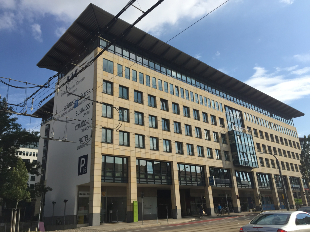 Großes modernes Gebäude mit zahlreichen Fenstern, beschriftet mit "Stadthalle Center for Business", umgeben von Bäumen und städtischer Infrastruktur in Köln, Deutschland.
