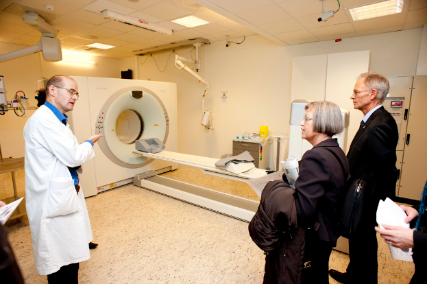 Ein Arzt in Weiß erklärt einer Person in Schwarz eine CT-Scan-Maschine.