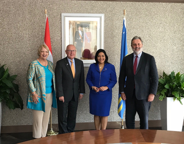 Eine Gruppe von Menschen, die um einen Tisch mit Papieren stehen, umgeben von Fahnen, Topfpflanzen und einem gerahmten Foto an der Wand, was die Unterzeichnung eines U.S.-Kanada-Memorandums von Verstehen darstellt.