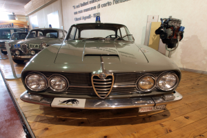 Ein klassischer Alfa Romeo Giulietta Sprint GT Junior aus den 1970er Jahren wird in einem Museum mit Seilabsperrungen und Wandtext exhibited.
