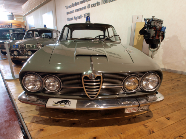 Ein klassischer Alfa Romeo Giulietta Sprint GT Junior aus den 1970er Jahren wird in einem Museum mit Seilabsperrungen und Wandtext exhibited.