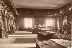 Ein altes Schwarz-Weiß-Foto eines Raumes voller Tische, Stühle, Skulpturen an den Wänden, Fenstern, Vorhängen, Geländern und anderen Gegenständen, mit Text unten lesend "Das Museum of Fine Arts, London".