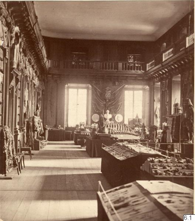 Ein altes Schwarz-Weiß-Foto eines Raumes voller Tische, Stühle, Skulpturen an den Wänden, Fenstern, Vorhängen, Geländern und anderen Gegenständen, mit Text unten lesend "Das Museum of Fine Arts, London".