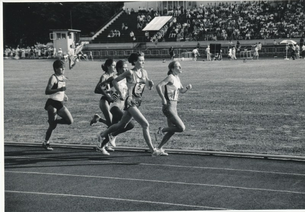 Schwarzes Bild von Frauen, die auf einer Laufbahn laufen, mit Zuschauern in den Rängen.