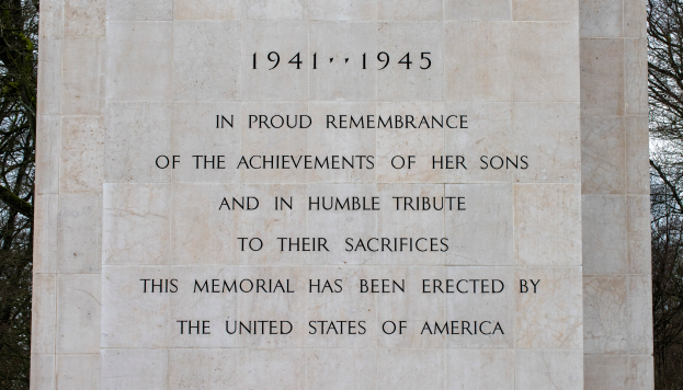 Ein Denkmal mit einer Tafel, auf der "In stolzem Gedenken an die Taten ihrer Söhne und in bescheidener Ehrung ihres Opfers" steht, vor einem Hintergrund aus Bäumen und einem klaren blauen Himmel.