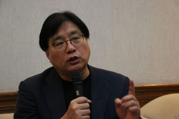 Mann im Anzug und mit Brille spricht in ein Mikrofon vor einer Wand.