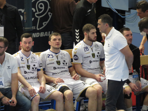Eine Gruppe von Männern sitzt auf einer Bank, einige halten Flaschen, im Hintergrund ist eine Fahne mit der Aufschrift "Nordkraque vs Bordeaux" zu sehen.