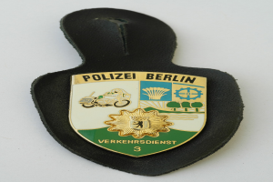 Ein schildförmiges Polizeibadge mit "Polizei Berlin" in schwarzer fetter Schrift, das ein weißes Stern auf einem blauen Hintergrund und einen weißen Rand hat, auf einer Oberfläche platziert.