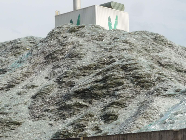 Großer Haufen Plastikmüll auf einer Zementwand mit einem Gebäude und einem klaren blauen Himmel im Hintergrund.
