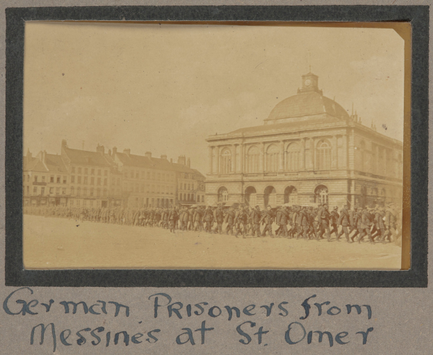 Gruppe deutscher Gefangener aus Messines vor einem Gebäude mit einem klaren blauen Himmel im Hintergrund, sichtbarer Text unten.