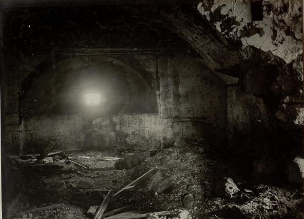 Ein Schwarz-Weiß-Foto eines zerfallenden Tunnels in den Ruinen der Berliner Mauer, mit einem Licht am Ende und Schutt auf dem Boden.