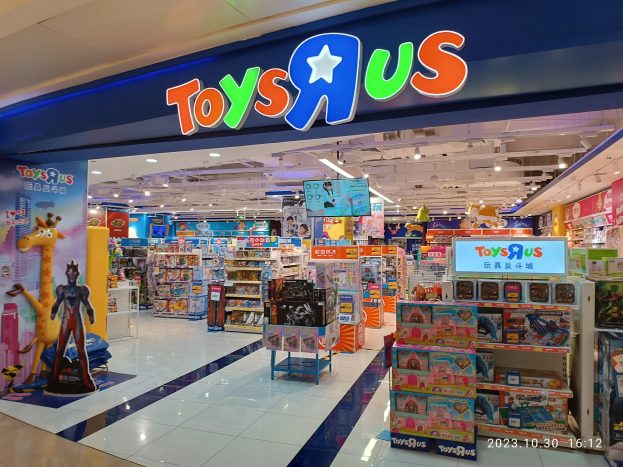 Ein Toys R Us Geschäft in einem Einkaufszentrum mit Regalen voller Spielzeug, ein Schild mit Text, Deckenleuchten und ein Wasserzeichen in der rechten unteren Ecke.