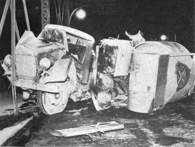 Ein Schwarz-Weiß-Foto eines umgestürzten Autos aus den 1930er Jahren neben einer Straße, mit Metallstangen und einem Laternenpfahl im Hintergrund.
