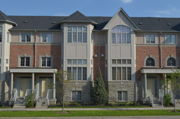 Eine Reihe von Stadthäusern in einer Wohngegend mit sichtbaren architektonischen Details, Grünfläche und einer Straße im Vordergrund vor einem Himmel-Hintergrund.