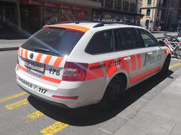 Ein weißer und oranger Polizeiwagen, der auf einer Straße geparkt ist, mit Fahrrädern auf dem benachbarten Gehweg und Menschen, die auf dem Bürgersteig im Hintergrund gehen.