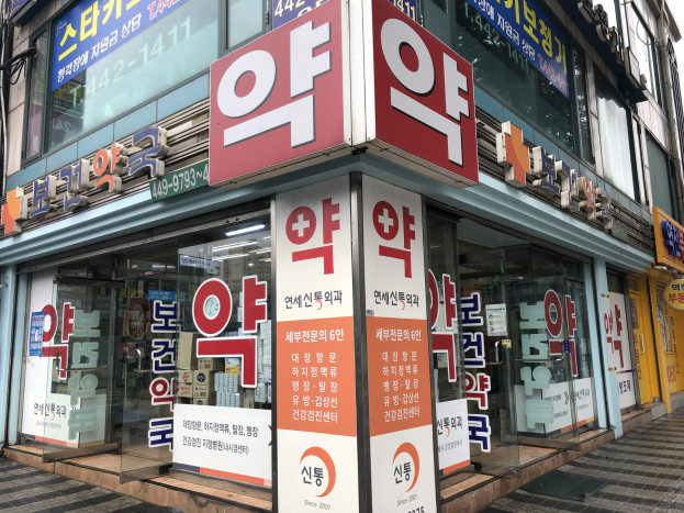 Außenansicht einer modernen Glaswand-Apotheke in Seoul, Südkorea, mit Texttafeln, die sie als die erste Apotheke der Stadt identifizieren.