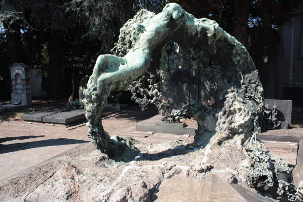 Ein Friedhof mit zahlreichen Gräbern umgeben von vielen Bäumen und einer Skulptur im Vordergrund.