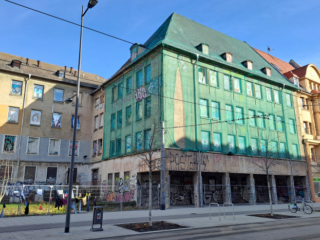 Ein großes grünes Gebäude in Berlin, Deutschland, mit Graffiti geschmückt, umgeben von Straßeninfrastruktur, Fahrzeugen, Fußgängern und Bäumen, als Teil des Berlin Wall Projekts.