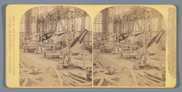 Ein altes Schwarz-Weiß-Foto einer Fabrik mit einem großen Geschütz in der Mitte, umgeben von mehreren anderen Geschützen, Metallstangen und verschiedenen Gegenständen auf dem Boden, mit Text auf der linken Seite.