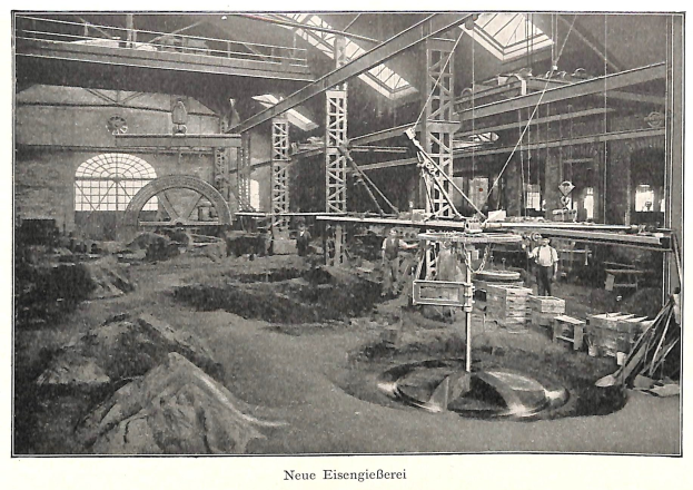 Schwarzes und weißes Foto einer Fabrik mit Arbeitern, die Maschinen bedienen, umgeben von Metallstangen und Pfählen, mit der Beschriftung "Neue Eisenglebeerei, die erste Fabrik in Deutschland" unten.