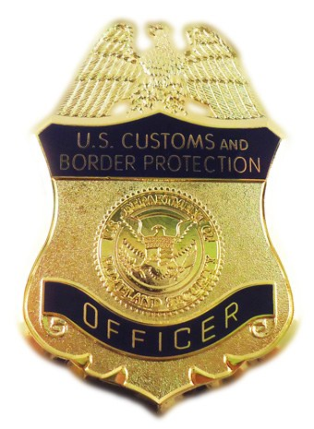 Goldes Abzeichen mit 'U.S. Customs and Border Protection Officer' eingraviert, mittig auf einem weißen Hintergrund.