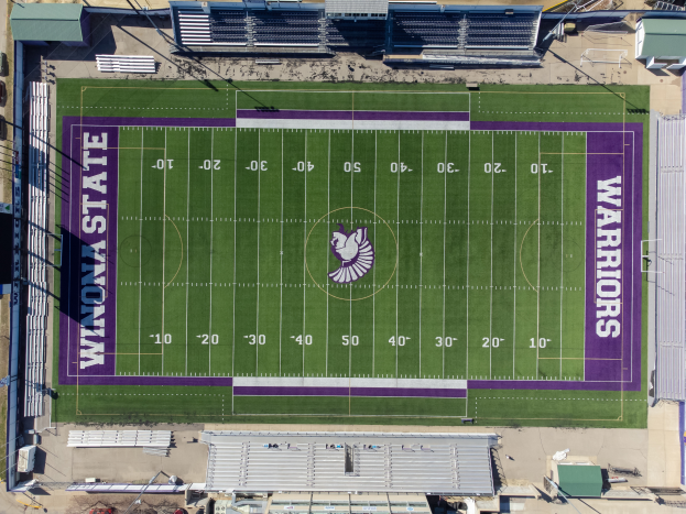 Eine Luftaufnahme eines Footballfelds mit violetten und weißen Markierungen, umgeben von Gebäuden, Fahrzeugen und anderen Gegenständen, die darauf hinweisen, dass es das Zuhause der Footballmannschaft der Minnesota State University ist.