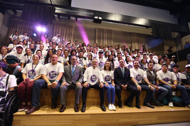 Eine Gruppe von Menschen sitzt auf einer Bühne mit einer Person im Rollstuhl links, vor einem Vorhang, Scheinwerfern und einer Wand auf einer NBA-Frauenbasketballkonferenz.
