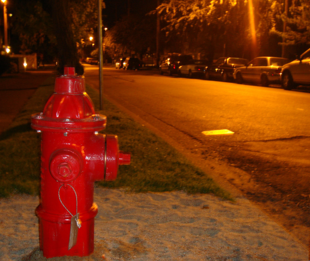 Ein Feuerhydrant an der Seite einer Straße, mit mehreren Autos und Bäumen in der Nähe.
