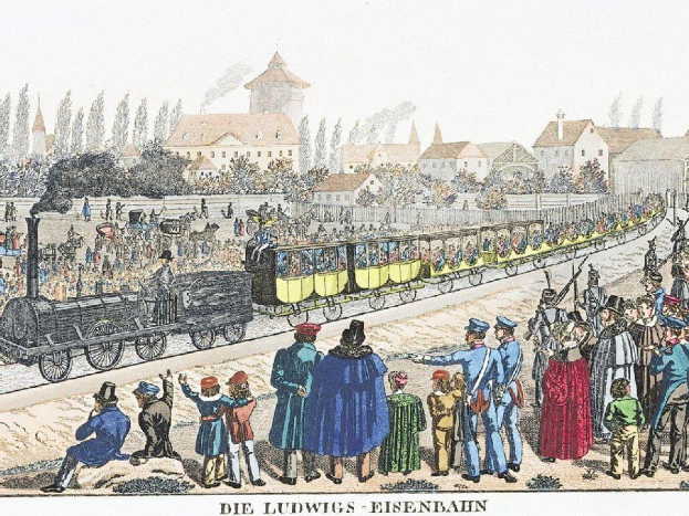 Eine Gruppe von Menschen, die um und in der Nähe eines Zuges auf einem Gleis stehen, einige sitzen im Zug und andere auf dem Boden, vor Gebäuden und Bäumen im Hintergrund, mit Text unten: "Ludwigs-Eisenbahn, die erste Bahnstation in Deutschland".