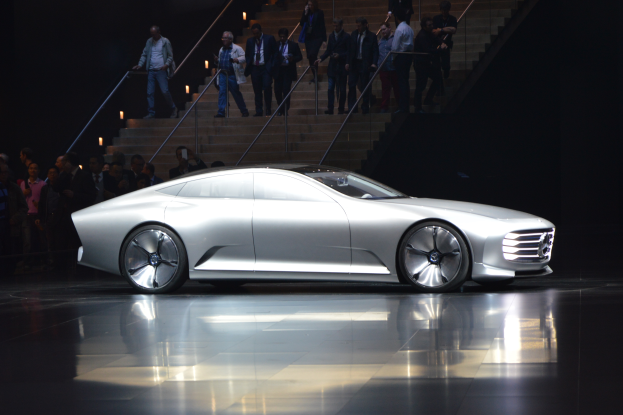 Ein Mercedes-Benz F 015 Luxury in Motion Concept-Auto, glänzend schwarz mit Chromakzenten, auf einem Boden mit einer Gruppe von formell gekleideten Menschen im Hintergrund.