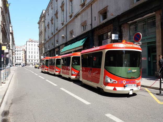 Eine Reihe roter und weißer Busse, die entlang einer Straße in Lyon, Frankreich, geparkt sind, mit Fußgängern auf dem benachbarten Gehweg und Gebäuden, die die Straße säumen.