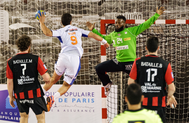 Eine Gruppe von Männern, die Handball spielen, mit einem, der springt und den Ball hält, vor einem Torpfosten und einer Fahne mit der Aufschrift "Ligue 1 - Bordeaux vs Marseille."