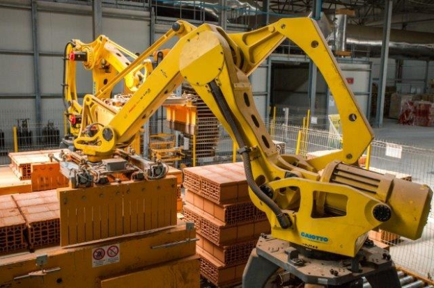 Großes industrielles Lagerhaus mit gestapelten Kisten, Überhead-Kränen, Zaun, Pfählen und einer entfernten Wand in einer automatisierten Fertigungsumgebung.