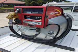 Ein Lastwagen mit einer Gasleitung am Heck, umgeben von Bäumen, einem Haus und einem klaren blauen Himmel.