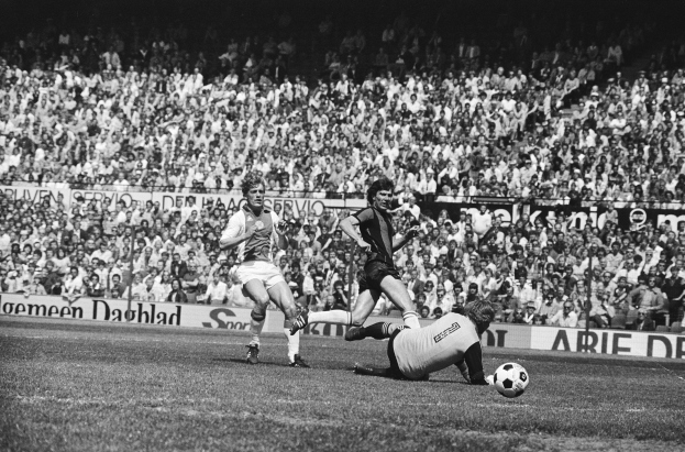Eine Gruppe von Männern, die Fußball spielen, auf einem Feld mit Zuschauern im Hintergrund und einem Banner mit der Aufschrift 'Bundesliga 1978-79 Ajax 1-1 Hannover 96' in Schwarz-Weiß.