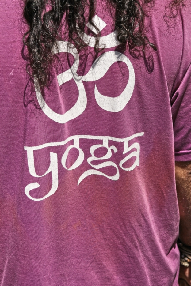 Eine Person in einem pinken T-Shirt mit der Aufschrift 'YOGA' und einem Symbol darauf, mit sichtbaren Haaren auf dem Kopf.